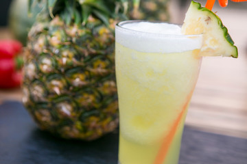 yellow pineapple smoothie with straw in a tall glass decorated with a piece of pineapple