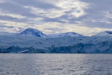 Fototapeta na wymiar Glacier front in antarctic sea with light reflections on dark ocean and cloudy sky, Antarctica