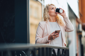 Businesswoman standing in front of building and drinking coffee