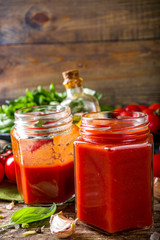 Fototapeta na wymiar Homemade tomato sauce with basil, garlic and fresh tomatoes. Ketchup, marinara sauce in small jars. On a wooden background, with fresh vegetables and basil.