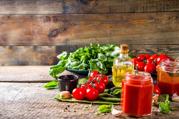 Homemade tomato sauce with basil, garlic and fresh tomatoes. Ketchup, marinara sauce in small jars. On a wooden background, with fresh vegetables and basil.