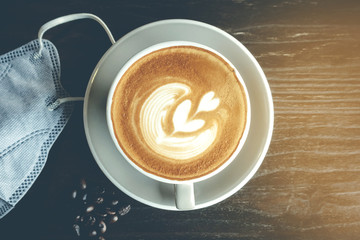 Hot Cappuccino coffee with  protective mask on a wooden table. Concepts of Flu virus, Covid-19 (Coronavirus disease).