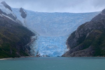 Glacier in chilean fjord with blue ice, high mountain and clouds, glacier alley, Beagle Channel