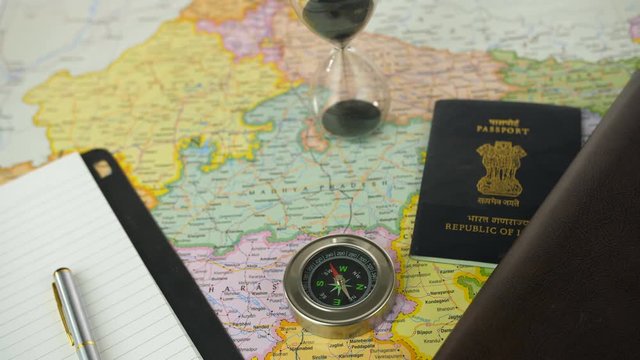 Pan shot of different travel accessories for planning a travel vacation to India. Closeup shot of an Indian political map placed with a travel diary  pen  sand clock  compass  wallet  and a passport