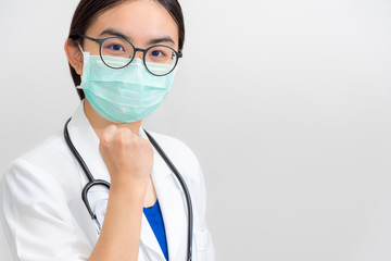 Beautiful Asian young woman doctor in white uniform and mask protect Coronavirus, Physician raise fist to support patient in the fight against disease epidemic COVID 19, gray copy space background