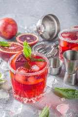 Skinny blood orange basil lemonade cocktail, with fresh bloody oranges, basil leaves and vodka, Grey stone concrete background flat lay copy space