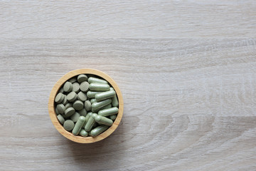 Herbal extract medicine tablets pills and capsules or Fa thalai chon (Andrographis Paniculata), Acanthaceae in wooden bowl on wooden background, Medical and healthcare concept