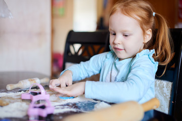 Red-haired girl cuts out cookie dough molds in the kitchen