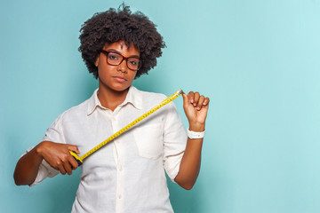 Black young woman with glasses and black power hair wearing a light shirt wearing a measuring tape