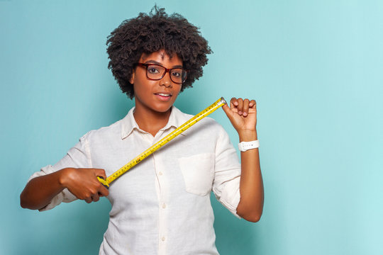 Black Young Woman With Glasses And Black Power Hair Wearing A Light Shirt Wearing A Measuring Tape