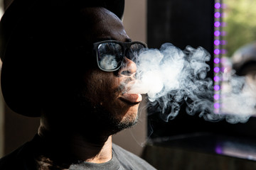 Black man with sunglasses and a vintage hat pulling smoke out of a steamer's mouth