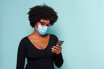 black woman with black power hair wearing protective mask with smartphone in hands and wearing reading glasses