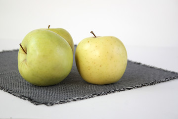 Three green apples lie on a checkered napkin. Light background. Close-up.