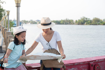 looking away. Outdoor portrait of two girls traveling around new place and searching beautiful sights. wonderful inspired curly woman in hat holding pretty daughter and town by the river map...