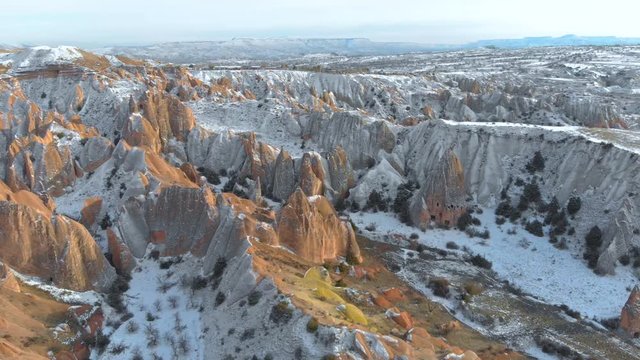 Aerial snowy landscape of Red Valley and Rose Valley at sunset in Cappadocia, Turkey. Aerial cinematic view of Tufa and rock formations covered with snow at Red Valley in Cappadocia.