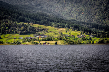 Traditional Norwegian houses near the lake with green forest on mountains on background..
