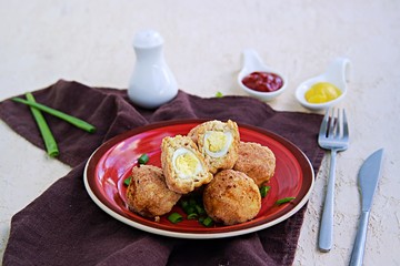 Scottish eggs, boiled quail eggs in minced chicken on a red clay plate on a light concrete background. Can be served as a starter or main course. Recipes with eggs.