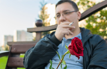 red rosebud in hand and against the background of a thoughtful guy who is waiting for a girl on a...