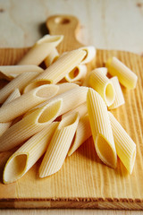 Dried penne pasta on wooden background 