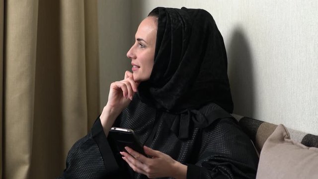 Young asian muslim woman in head scarf smile. Beautiful middle eastern woman wearing abaya. Arabian woman with happy smile. Playing with mabile phone.