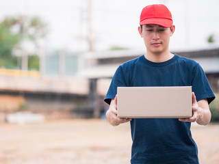 Asian Delivery Man Wearing Red Cap Holding Parcel Box in Outdoor Setting
