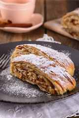 Pieces of delicious strudel stuffed with apples and cinnamon at a plate near cup, vertical orientation