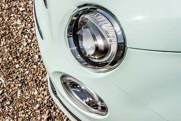 Headlight and fog light seen on a new, Italian-made supermini. Showing the new design headlight structure, seen on a gravel driveway. The classic aqua coachwork is seen.