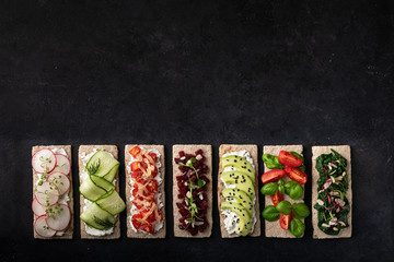 Different kinds of vegetarian sandwiches on a black background. Top view, place for text.