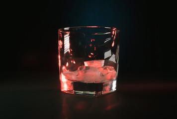 Szklanka z lodem na czarnym tle w czerwonych refleksach.