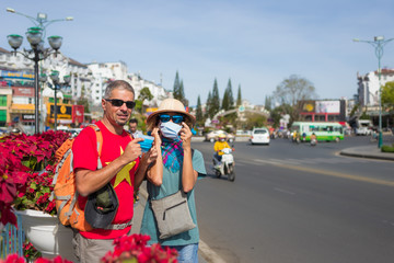 Obraz na płótnie Canvas Caucasian woman and man wearing sanitary mask outdoors in Da Lat city centre Vietnam. Tourist couple with medical mask protection against risk of covid-19 flu virus epidemy in Asia.