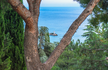 Lighthouse on the embankment of Yalta visible through the trees from the hill
