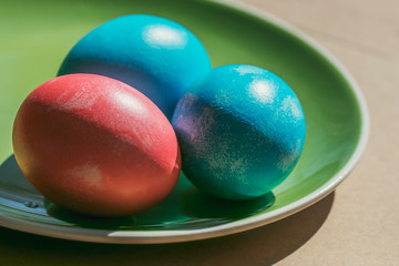 Easter photo from Russia. Chicken eggs are painted in blue and pink according to ancient tradition, lie on a green ceramic plate. Retro style still life in the spring sunshine.