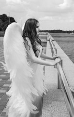 A beautiful girl with long hair in the image of an angel with white wings stands on the background...
