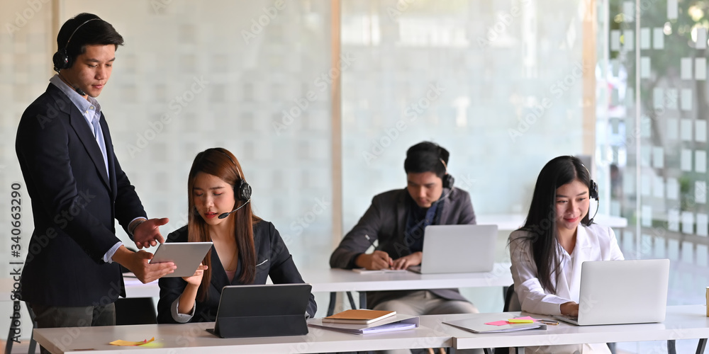 Poster call center/operator/call service team while working and sitting together at the long working desk o