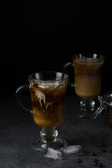 Two glasses of iced coffee with cream stand on the table on a dark background.