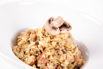 Risotto with button mushroom and bacon decorated with mushroom on a plate on a white background