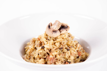 Risotto with button mushroom and bacon decorated with mushroom on a plate on a white background