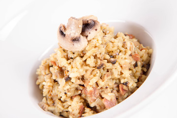 Risotto with button mushroom and bacon decorated with mushroom on a plate on a white background
