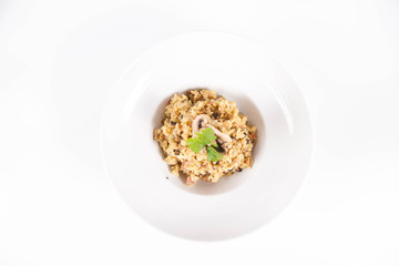 Risotto with button mushroom and bacon decorated with parsley on a plate on a white background