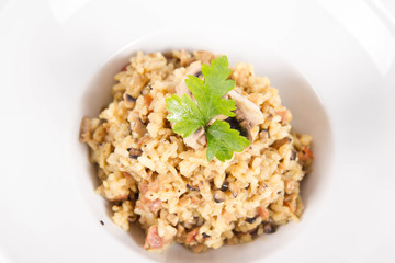 Risotto with button mushroom and bacon decorated with parsley on a plate on a white background