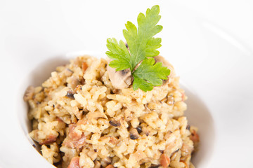 Risotto with button mushroom and bacon decorated with parsley on a plate on a white background
