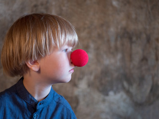 Portrait of charming blond boy in blue shirt with red clown nose and blue ball