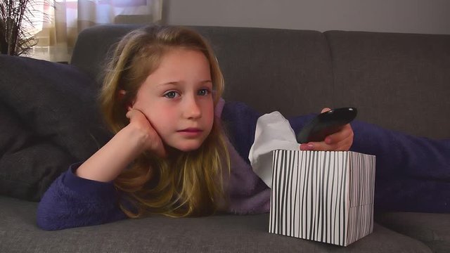 bored schoolgirl lies on couch and is switching TV channels with remote control