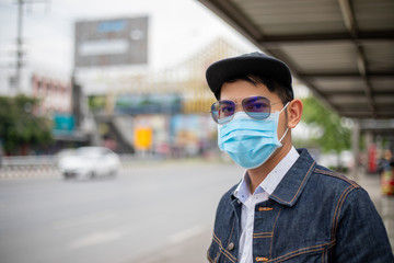 Fototapeta na wymiar Asian Young man standing in the city and wearing protection mask on face for protection air pollution, particulates and for protection flu virus, influenza, coronavirus at city