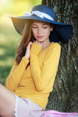 Jeune femme avec un chapeau de paille bleu souriante au pied d'un arbre