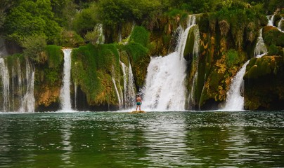 Fototapeta premium Waterfall in the nature with a young man flexing muscles. Green forest with a river. Near Plivice lakes in croatia