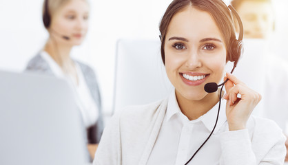 Call center in sunny office. Group of diverse operators at work. Beautiful woman in headset communicating with customers of telemarketing service. Business concept