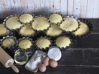 Concept of culinary background.Baking ingredients and raw rolls in molds on a dark wooden table with a white background.
