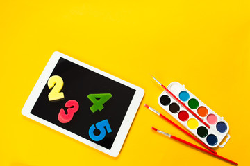 school paint supplies and tablet on a yellow isolated background, theme back to school