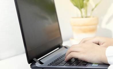 An Asian woman works from home using a single laptop on a white desk with a phone beside her.